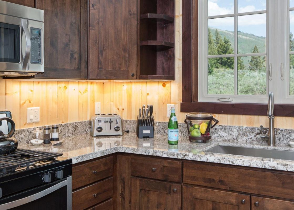A well-appointed kitchen in The Shooting Cabin features dark wood cabinetry, granite countertops, stainless steel appliances, and a window overlooking a mountain landscape.