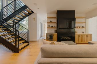 A modern living room with a fireplace, TV, and staircase at Three Peaks.
