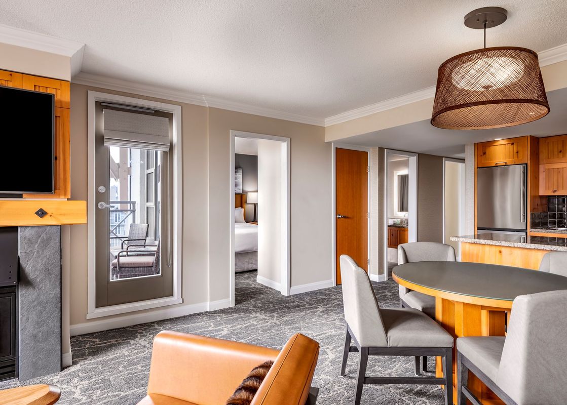 A spacious and elegantly furnished living area featuring a fireplace, a dining table, and an open-concept kitchen, with a door leading to a balcony.