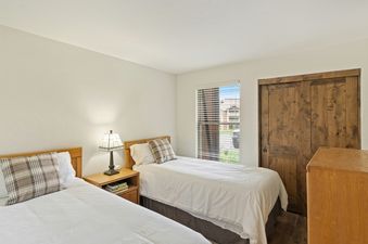 A bedroom with two twin beds, a wooden nightstand with books, and a lamp.