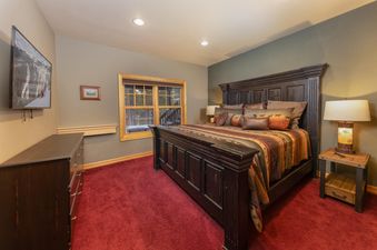 A master bedroom at Baldy Ridge Chalet, featuring a comfortable bed with rustic bedding, a large dresser, and a window offering a view of the surrounding trees.