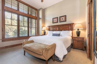A bedroom with a king-sized bed and a large window with blinds.