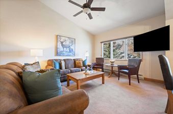 The living room of The Charter F4405 features a comfortable seating area with brown leather sofas, a wooden coffee table, and large windows revealing a scenic winter mountain view.