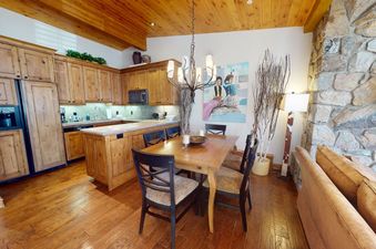 The dining area of Manor Vail 227 features a wooden table with six chairs and a chandelier above.