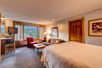 A hotel room with a bed, couch, and a view of the mountains outside the window.