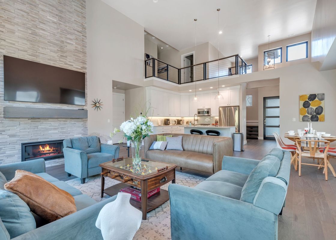 Spacious double-height living room in Mayflower Lakeside 9975 featuring a stone fireplace, plush blue seating, and an open kitchen and dining layout.