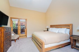 A cozy bedroom in Cimarron Lodge 35 with a wooden bed, beige bedding, a large dresser with a TV, and a glass door leading to a balcony.