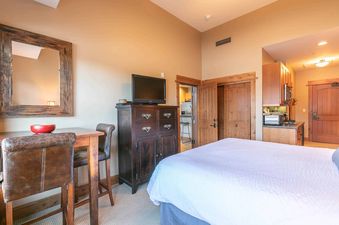 A hotel room with a bed, a dresser, and a small kitchen area.