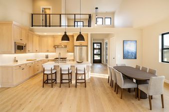 A modern kitchen and dining area in the Keetly Vista with light wood cabinetry, stainless steel appliances, an island with seating, and an oval dining table.