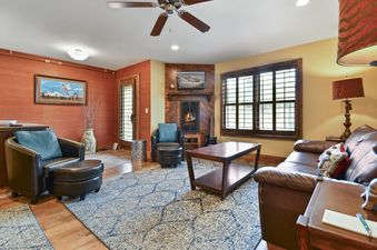 A cozy living room in The Pearl of Park City featuring a central fireplace with a warm glow, comfortable leather seating, and a decorative blue and white rug.
