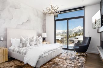 The luxurious bedroom at Moonlight Basin 8C Speedwell features a plush king-sized bed, a cozy armchair, and a fireplace, all with breathtaking views of the mountains outside.