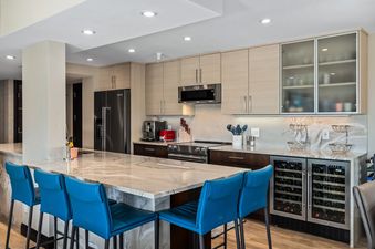 A modern, fully-equipped kitchen with a large marble island and vibrant blue barstools.