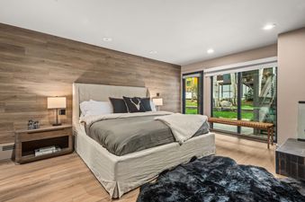 A luxurious bedroom at Timber Ridge 1B features a large bed, wooden accent wall, and expansive windows offering views of the lush outdoors.