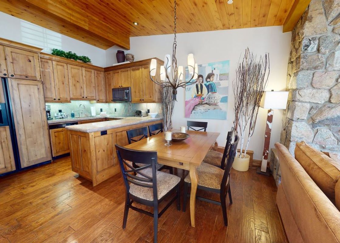 The dining area of Manor Vail 227 features a wooden table with six chairs and a chandelier above.