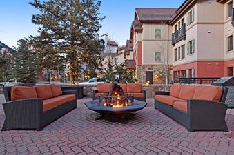 Outdoor fire pit area with seating, a lit fire and a view of a condo building