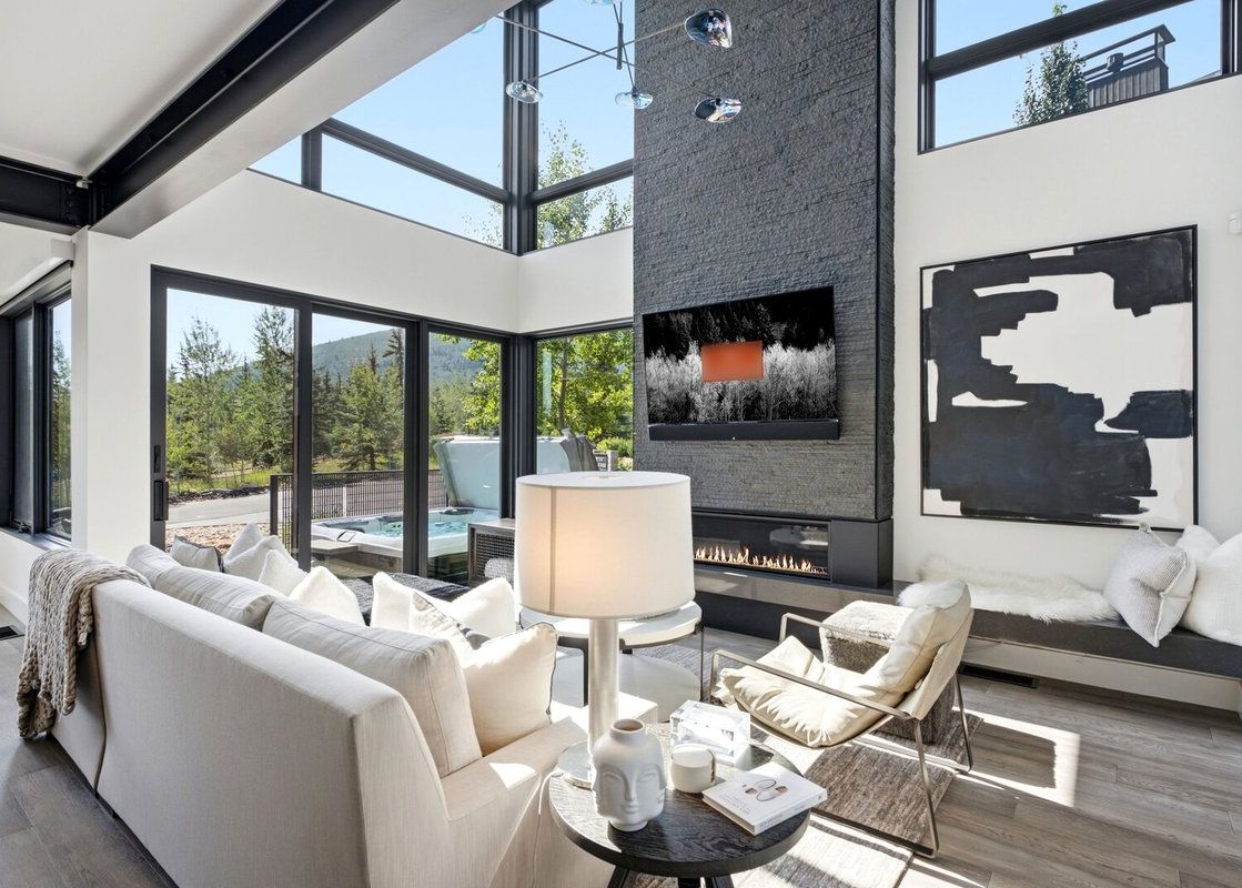 A bright, double-height modern living room at The Ridge at Canyons Village with a stone fireplace, large windows, and an outdoor hot tub view.