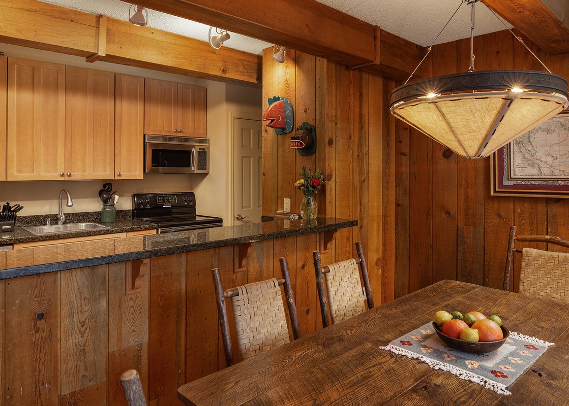 A cozy kitchen and dining area with wooden furnishings and rustic decorations, bathed in warm lighting.