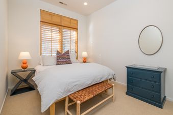A bedroom with a white bed, a wooden bench at the foot of the bed, and a blue dresser with three drawers.