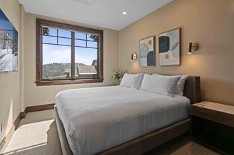 A peaceful bedroom at Silver Strike Lodge 706 features a large bed with white bedding, abstract art, and a big window overlooking a mountain landscape.