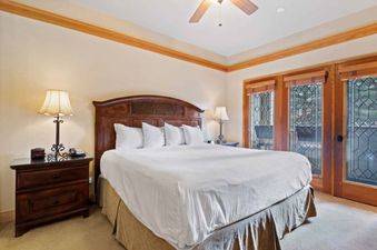 A king-sized bed with a wooden headboard, white bedding, two nightstands with lamps, and double glass doors with decorative leaded glass patterns.