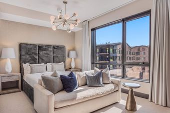 The luxurious bedroom at One Snowmass East 704 featuring a large bed, stylish sofa, and expansive windows.