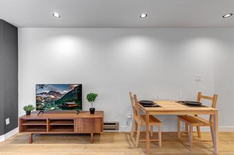 A modern dining and entertainment area at Snowcrest 216 featuring a wooden TV console with a TV displaying a mountain lake, potted plants, and a light wooden dining table set for two with matching chairs.