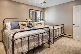 A cozy bedroom at Ranch at Steamboat RA407 featuring two full-size beds with dark metal frames, plaid bedding, and moose-themed throw pillows, overlooking an outdoor view through a large window.