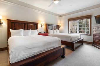 A hotel bedroom at The Charter D340 with two queen beds, dark wooden furniture, and a window overlooking a snowy landscape.