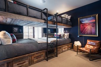 A cozy bunk room at Silver Star 40 with custom-built bunk beds, gray bedding, dark blue walls, and a vibrant landscape painting.