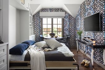 A cozy bedroom with patterned wallpaper, a comfortable bed, a dining nook, a TV, and built-in storage.