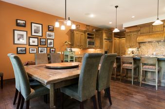 The dining room and kitchen of Silver Star 15 are shown with wooden furniture, warm orange walls adorned with framed pictures, and a fully equipped kitchen with wooden cabinetry.