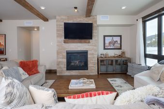 A cozy and rustic living room with a fireplace, television, comfortable sofas, and a view of snow-covered mountains.