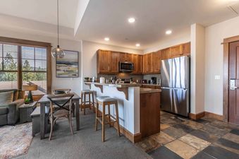 A kitchen with stainless steel appliances, wood cabinets, and a breakfast bar with two stools.