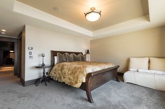 A luxurious master bedroom at Harmony Haus featuring a large sleigh bed with floral bedding, a chaise lounge, and warm lighting.