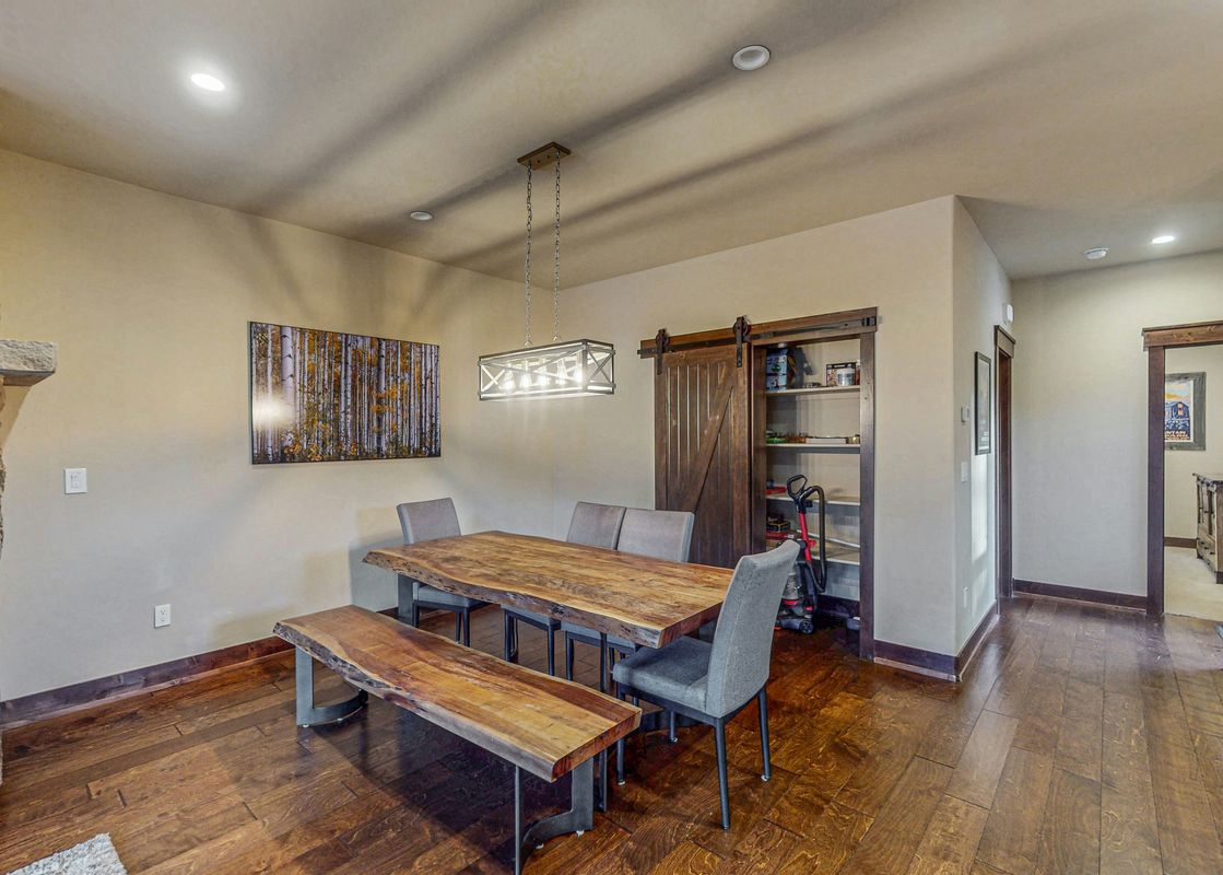 The dining area in Keystone Townhome features a large wooden table and bench, with a modern chandelier overhead.