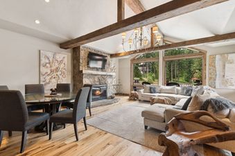 A bright and spacious open-concept living area with hardwood floors, vaulted ceilings, a stone fireplace, and a large window overlooking a lush green landscape.