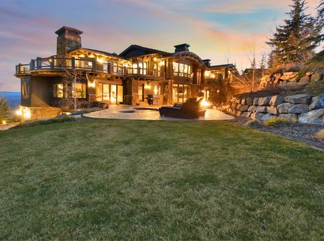 An evening view of the Ski Dream Home, showcasing its illuminated exterior, multiple balconies, a patio with a fire pit, and a well-maintained lawn.