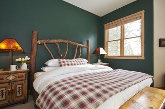 Cozy bedroom in Moose Creek 30 with a rustic log headboard, green walls, and a plaid blanket.