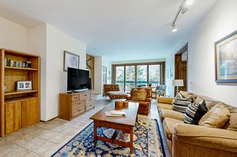 The living room of SunRiver E101 has a couch and an armchair, a coffee table, a bookshelf, and a television.