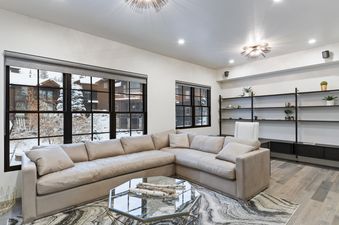 A modern living room with a large cream sectional, a geometric glass coffee table, and windows overlooking a snowy landscape.