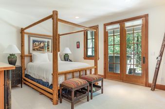 A rustic master bedroom with a wooden four-poster bed and French doors leading to an outdoor deck.