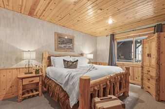 The well-appointed bedroom in Black Bear 207 features a rustic wooden bed frame, matching bedside table, and wood-paneled walls.