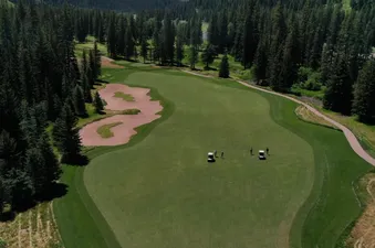 An aerial view of The Sylvan Lodge Two Bedroom Suite's golf course, featuring lush green fairways, sandy bunkers, and surrounding pine forests, with golfers and carts visible on the course.
