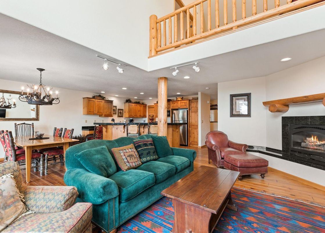 An expansive open-concept living space at Silvertip Ski Haus, showcasing a living room with a green sofa and fireplace, a dining area, and a kitchen under a loft.