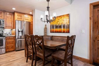 A rustic dining table and chairs with bench seating, an artistic painting of birch trees, and a kitchen with stainless steel appliances are shown in The Charter F2505.