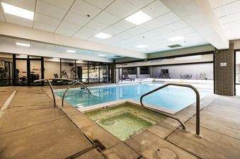 An inviting indoor pool and hot tub area at Resort Plaza 5051, featuring clear blue water, modern lighting, and an adjacent fitness center visible through glass walls.