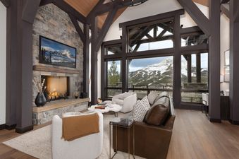 A cozy living room with a stone fireplace, large windows overlooking a snowy mountain, and comfortable seating.