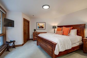 A cozy bedroom at Chateau Chamonix CX211 features a large wooden bed with white bedding, orange accent pillows, and a wall-mounted TV.