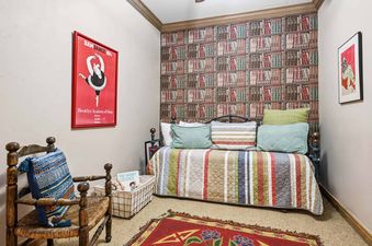 A cozy bedroom at Highlands Slopeside 222 features a daybed with a striped quilt, a rustic armchair, and a bookshelf-patterned accent wall, complemented by colorful art and rugs.