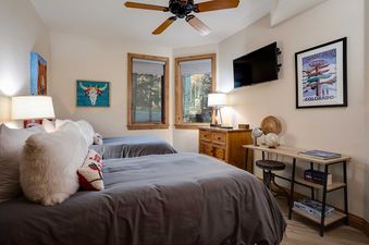 A cozy bedroom at Chateau Chamonix CX322 with two twin beds, a flat-screen TV, and decorative wall art, bathed in natural light from large windows.